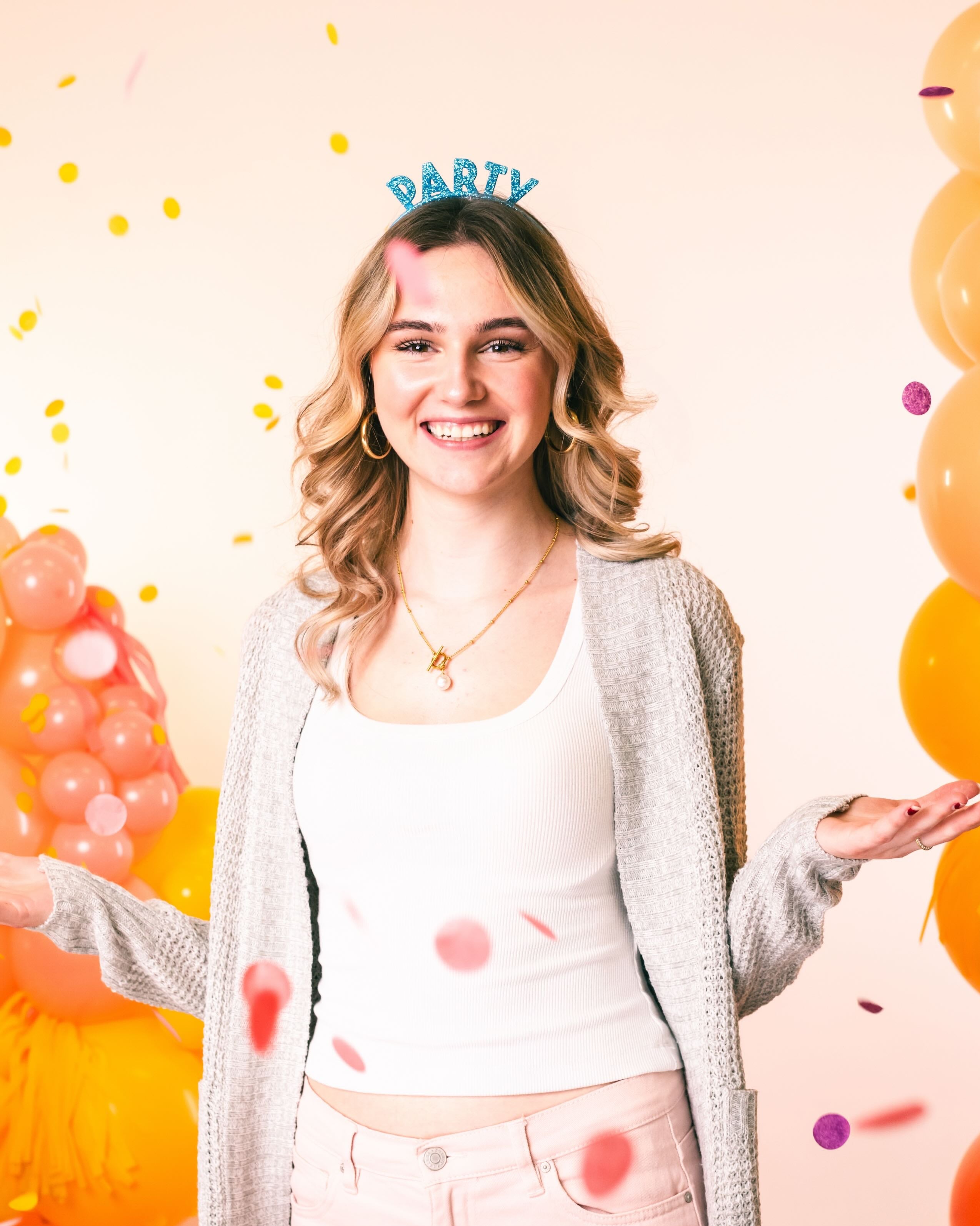 Woman smiling at the camera wearing a 'PARTY' headband with confetti and balloons in the background