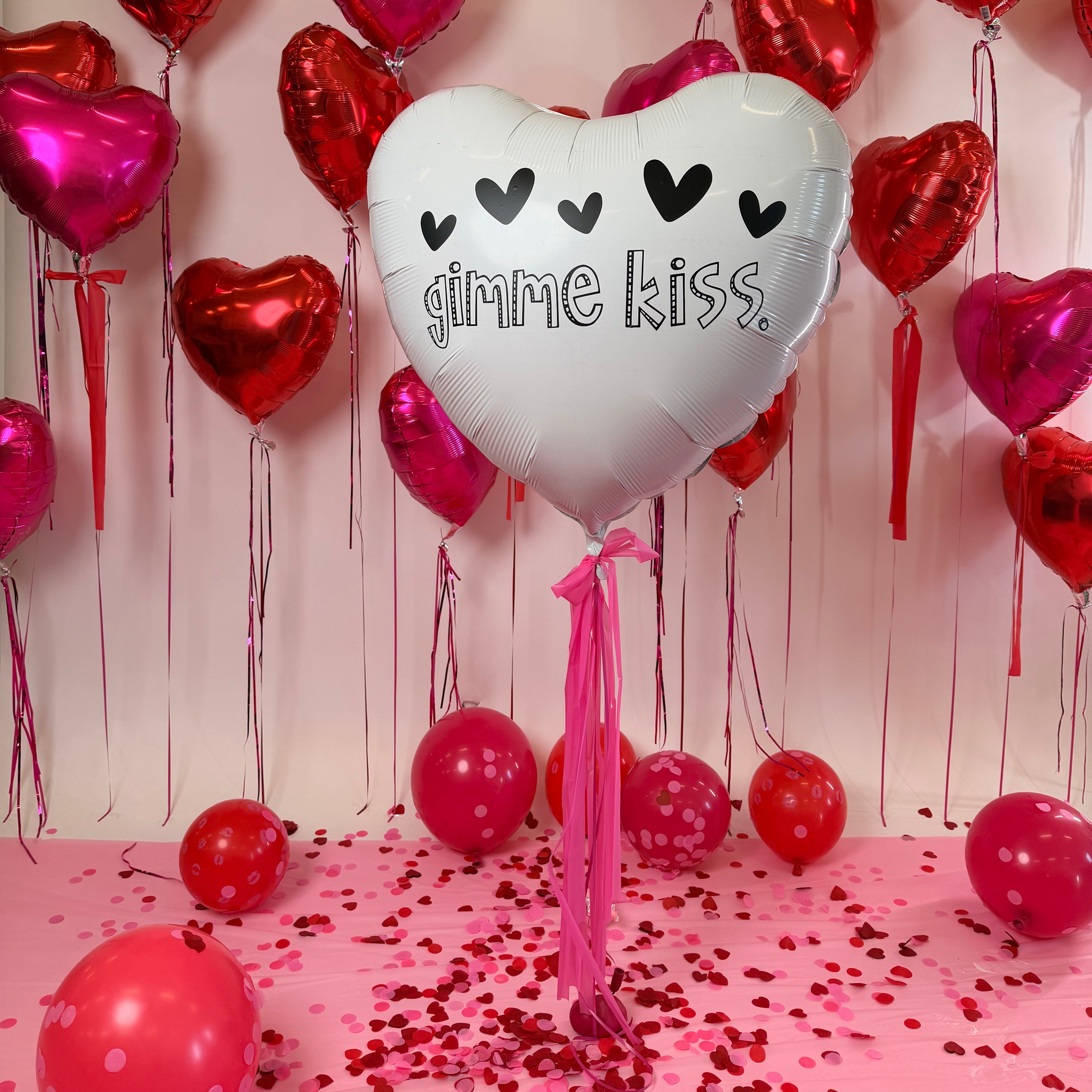 Heart-shaped balloons with a 'kiss' balloon on a pink background