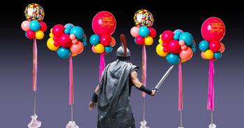 A man with a sword and knight armour stands in with his back facing the audience in front of a bunch of balloons