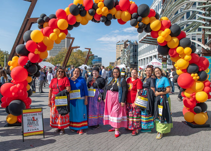 Indigenous women in their traditional dress pose under a balloon arch